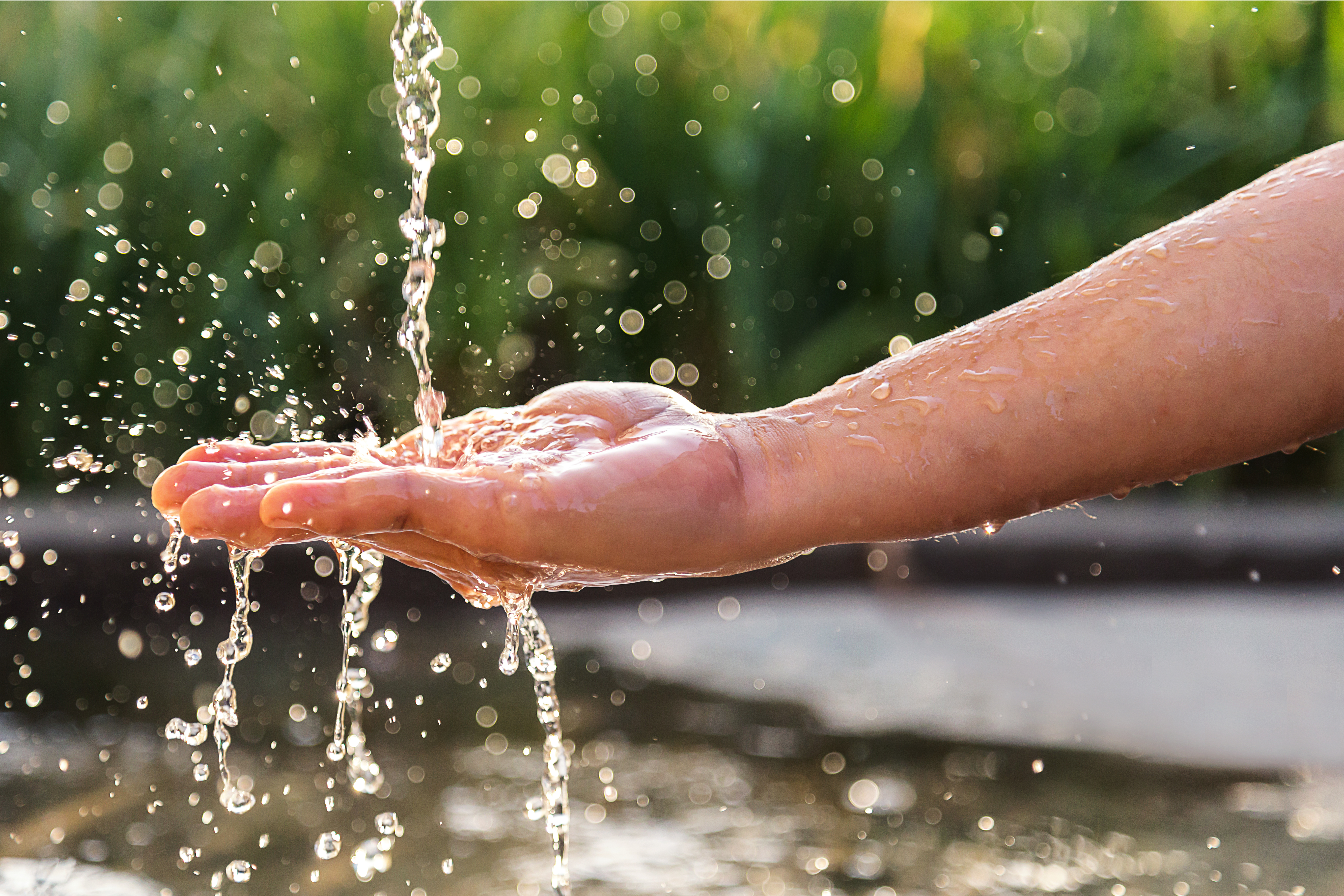 Hand outside near pond lake with water splashing over palm